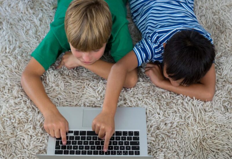 Dos ni&ntilde;os acostados en una alfombra usando un port&aacute;til